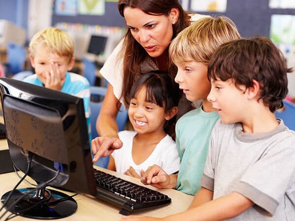 Business K 12 Education Library Solutions Features 600x450 School teacher helping kids in front of a computer