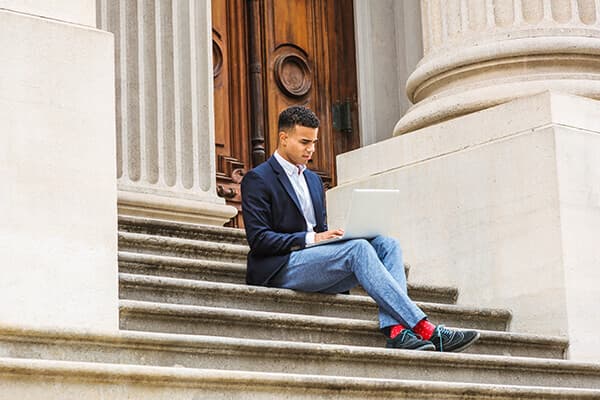 Business State and Local Gov Features 600x400 Man looking at phone sitting outside on stairs of government building